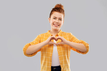 people concept - smiling red haired teenage girl in checkered shirt making hand heart gesture over...