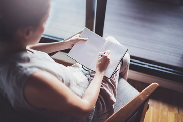 Working at home concept. Young business woman writing and taking notes while relax sitting in comfort chair at home. Preparing plans for next week.