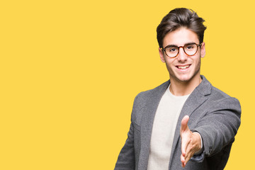 Naklejka premium Young business man wearing glasses over isolated background smiling friendly offering handshake as greeting and welcoming. Successful business.