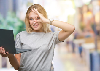 Young caucasian woman using computer laptop over isolated background with happy face smiling doing ok sign with hand on eye looking through fingers