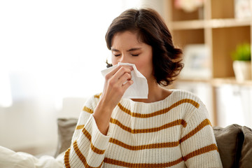 healthcare, cold, allergy and people concept - sick woman blowing her runny nose in paper tissue at home - obrazy, fototapety, plakaty