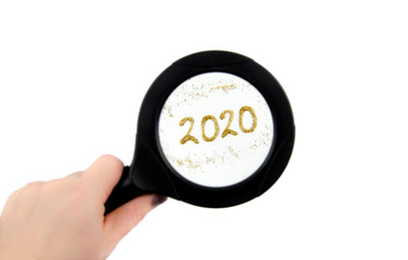 Hand holding magnifying glass and looking through, seeing year 2020 text. New year concept.
