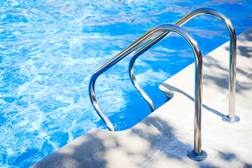 Staircase on the swimming pool edge with blue water copy space during a sunny summer day