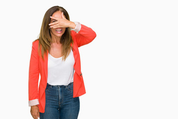 Beautiful middle age business adult woman over isolated background peeking in shock covering face and eyes with hand, looking through fingers with embarrassed expression.