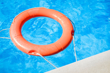 Closeup view of the swimming pool edge with blue water and a red ring life buoy floating on it during a sunny summer day