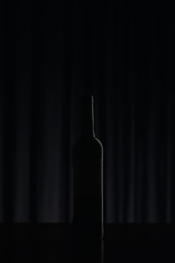 Silhouette of wine bottle on black surface in darkness