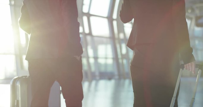 Rear on the Caucasian couple of co-workers going through the airport hall and carrying their suitcases on the wheels before the departure to the business trip. Rear. Camera moving down.
