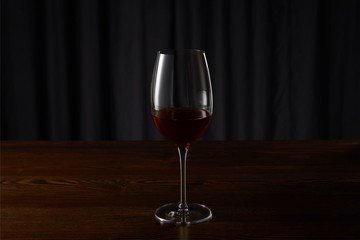 Glass with red wine on wooden surface on dark