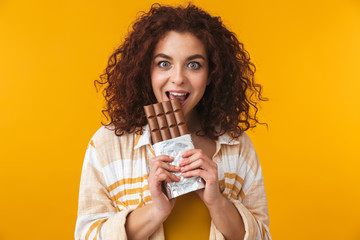 Beautiful young curly girl posing isolated over yellow wall background holding chocolate.