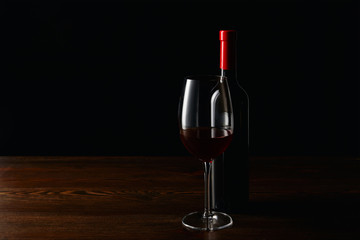 Fototapeta na wymiar Bottle and glass of red wine on wooden surface isolated on black