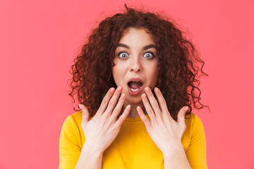 Shocked confused beautiful young curly girl posing isolated over red wall background.