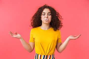 Happy beautiful young curly girl posing isolated over red wall background with bubble gum.
