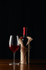 Wine glass and bottle in paper wrapper on wooden surface isolated on black