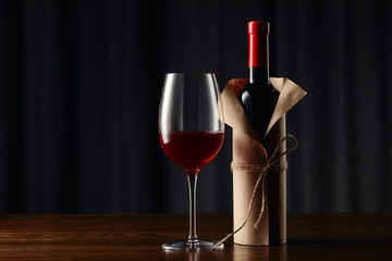 Wine glass and bottle in paper wrapper on wooden surface