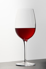 Wine glass with red wine on dark surface on white