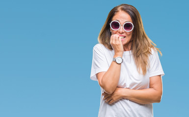 Middle age hispanic woman wearing fashion sunglasses over isolated background looking stressed and nervous with hands on mouth biting nails. Anxiety problem.