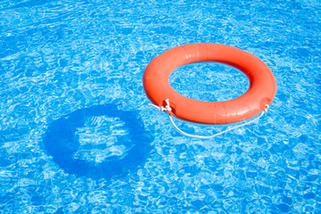 Closeup view of a red ring life buoy and its shadow floating on the blue water of the swimming pool during a sunny summer day