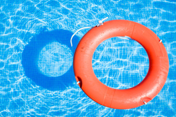 Closeup view of a red ring life buoy and its shadow floating on the blue water of the swimming pool during a sunny summer day
