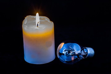 Burning candle and an electric light globe isolated on a black background image with copy space in...