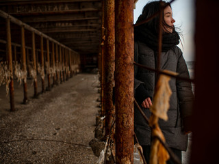 young girl in a coat stands near metal rusty structures near the sea coast