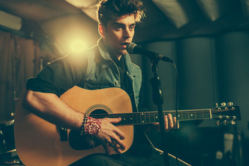 Obraz premium good-looking musician singing in microphone while playing acoustic guitar