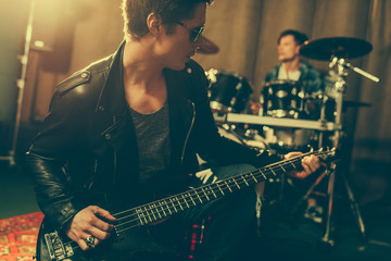 Obraz premium stylish guitarist in sunglasses playing electric guitar near drummer