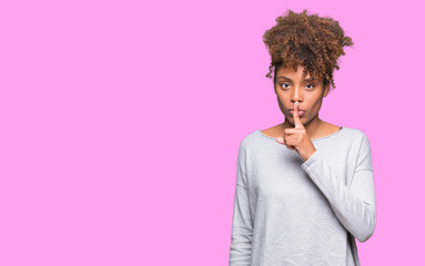 Beautiful young african american woman over isolated background asking to be quiet with finger on...
