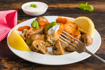 Tilapia fish fillet baked with vegetables, carrot, celery and mushrooms. White plate on wooden rustic table