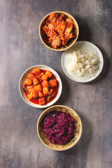 Variety of fermented food korean traditional kimchi cabbage and radish salad, white and red sauerkraut in ceramic plates over grey texture background. Flat lay, space