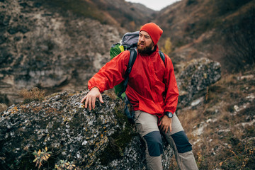 Outdoors portrait of tired hiker man in red clothes sitting on the rock relaxing after hiking in...