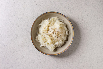 White sauerkraut chopped cabbage pickled in brine with cumin in ceramic plate over grey spotted background. Flat lay, space