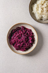 Obraz na płótnie Canvas Red and white sauerkraut chopped cabbage pickled in brine with cumin in ceramic plate over grey spotted background. Flat lay, space