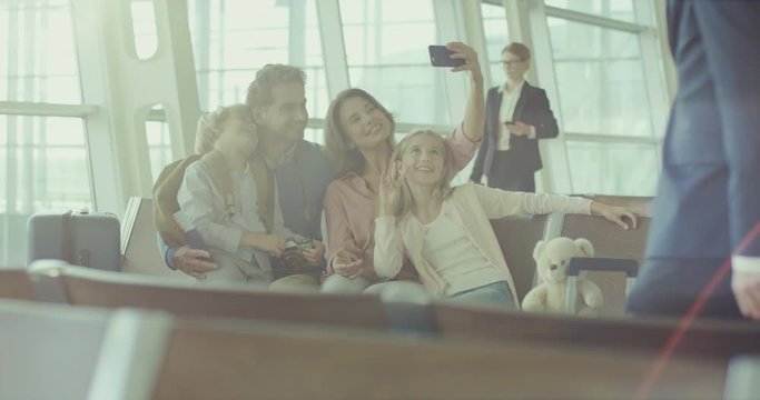 Happy smiled Caucasian parents with daughter and son taking a selfie photo with smartphone camera in the airport at the departure hall.