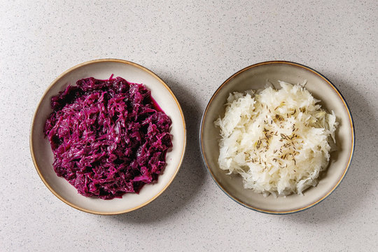 Red and white sauerkraut chopped cabbage pickled in brine with cumin in ceramic plate over grey spotted background. Flat lay, space