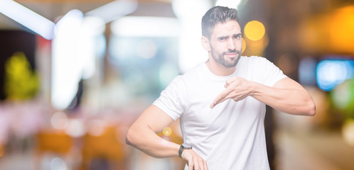 Fototapeta na wymiar Handsome man wearing white t-shirt over night outdoors background In hurry pointing to watch time, impatience, upset and angry for deadline delay