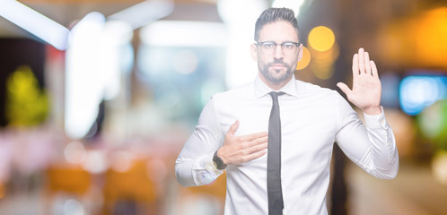 Young handsome business man wearing glasses over isolated background Swearing with hand on chest...