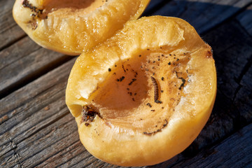 In one half of the apricot crawling malicious worm. On wooden boards is ripe apricot opened into two halves. The sun is shining, hot day. The fruit is ripe and juicy. Healthy food.