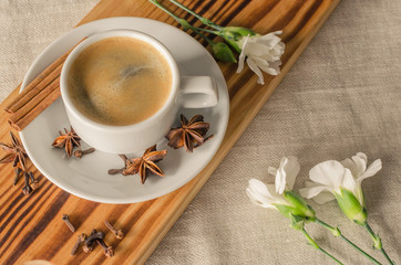 A cup of espresso, cinnamon sticks, anis stars and white carnations on wooden desk and textile...