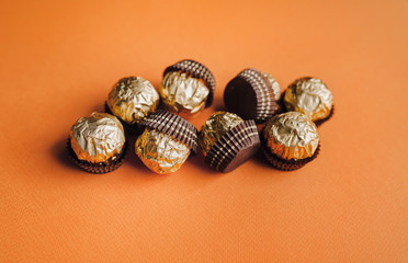 Round chocolates in brown paper baskets lie on an orange background.