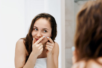 Young woman  looking and squeeze  acne on a face in front of the mirror. Ugly problem skin girl, teen girl having pimples. Skin care. Beauty