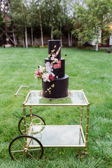 Closeup of black wedding cake with flowers. cake on the cake-shelf. Cake decorated with pink and purple flowers with gold details