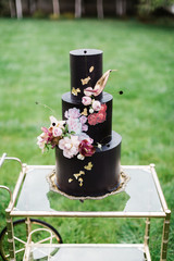 Closeup of black wedding cake with flowers. cake on the cake-shelf. Cake decorated with pink and purple flowers with gold details