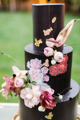 Closeup of black wedding cake with flowers. cake on the cake-shelf. Cake decorated with pink and purple flowers with gold details