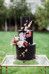 Closeup of black wedding cake with flowers. cake on the cake-shelf. Cake decorated with pink and purple flowers with gold details