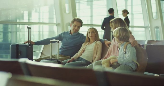 Beautiful and cheerful caucasian family of parents and two kids sitting with baggage in the airport at the department hall and talking.