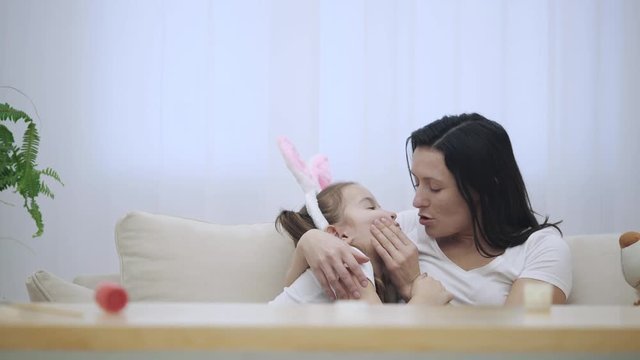 Daughter rushes into mother's arms at home and gives her a big hug. Happy parent is kissing her daughter.