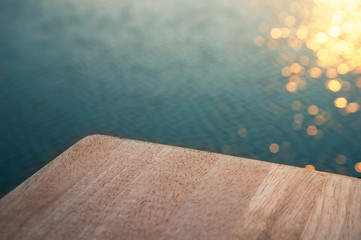 top of wood with blue lake water with orange sunset bokeh light for summer vacation background