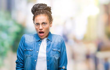 Obraz premium Young braided hair african american girl wearing glasses over isolated background afraid and shocked with surprise expression, fear and excited face.