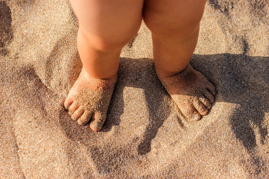 Baby feet walking on sand beach in the summer.
