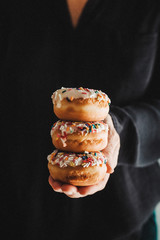 Female hands holding a pile of colorful donuts